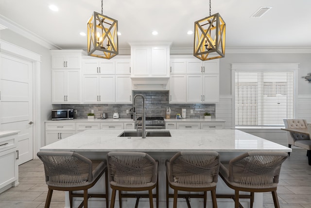 326 E Lakeshore Dr, Panama City Beach, FL 32413 - kitchen featuring appliances with stainless steel finishes, ornamental molding, backsplash, white cabinetry, and an island with sink