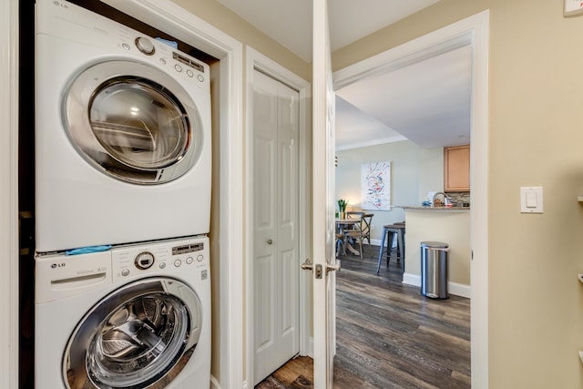 laundry room featuring ornamental molding, stacked washer / dryer, and dark wood-type flooring