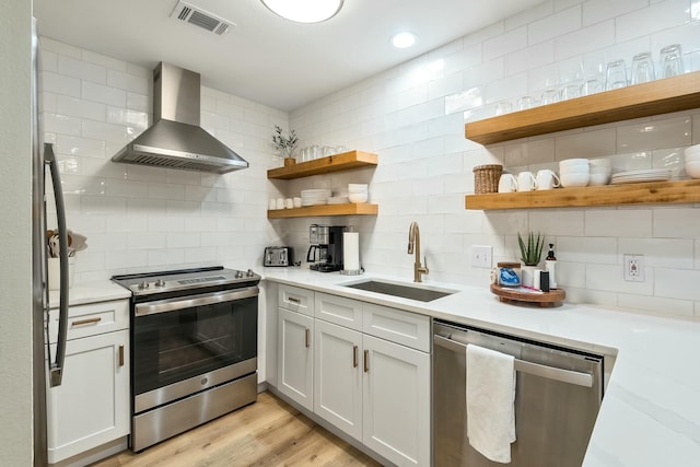 kitchen with white cabinetry, sink, wall chimney exhaust hood, appliances with stainless steel finishes, and light wood-type flooring