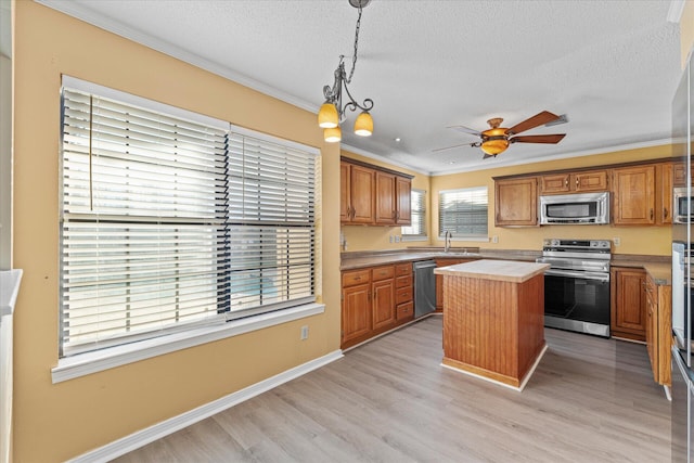 kitchen featuring sink, crown molding, decorative light fixtures, a kitchen island, and appliances with stainless steel finishes