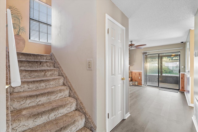 stairs with a textured ceiling, ceiling fan, and a healthy amount of sunlight