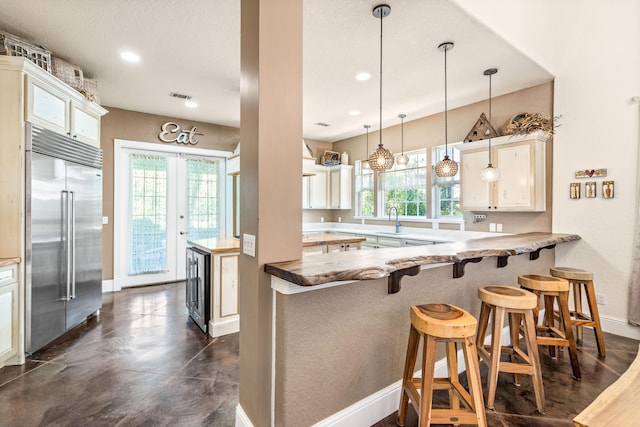 kitchen with a kitchen bar, kitchen peninsula, stainless steel built in fridge, and decorative light fixtures