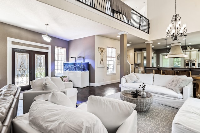 living room with french doors, a towering ceiling, an inviting chandelier, and ornate columns