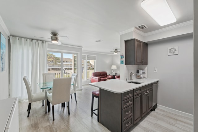 kitchen featuring dishwasher, sink, ornamental molding, dark brown cabinets, and kitchen peninsula