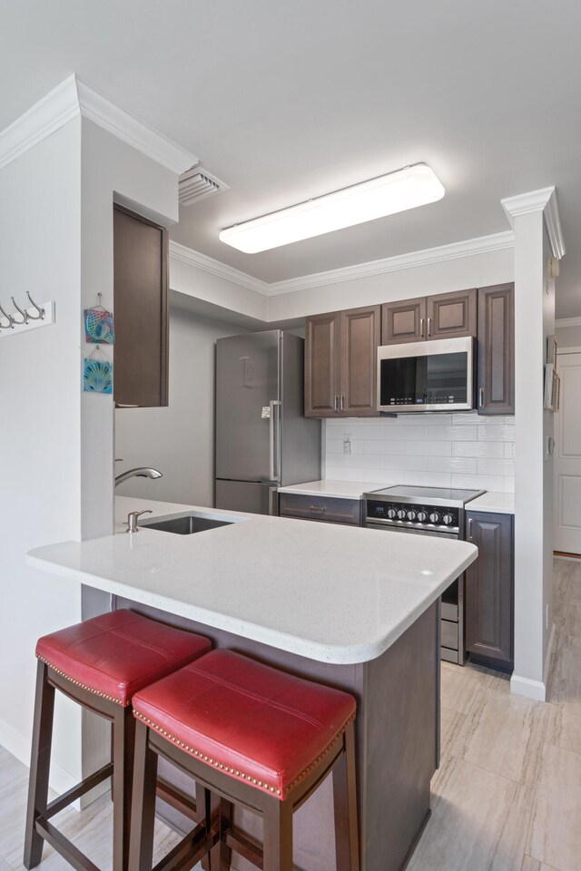 kitchen featuring a breakfast bar, stainless steel appliances, crown molding, and sink