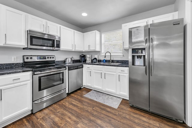 kitchen with appliances with stainless steel finishes, sink, dark stone countertops, dark hardwood / wood-style floors, and white cabinetry