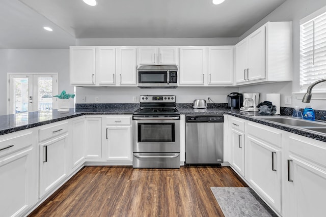 kitchen with appliances with stainless steel finishes, dark hardwood / wood-style flooring, sink, dark stone countertops, and white cabinets