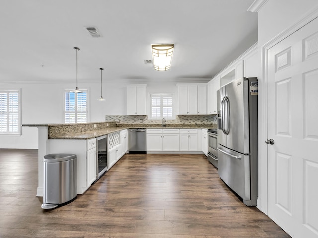 kitchen with kitchen peninsula, appliances with stainless steel finishes, pendant lighting, dark stone countertops, and white cabinets