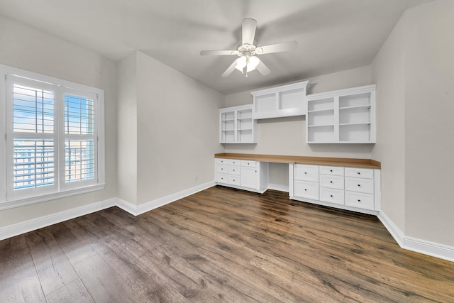 unfurnished office featuring dark hardwood / wood-style floors, ceiling fan, and built in desk