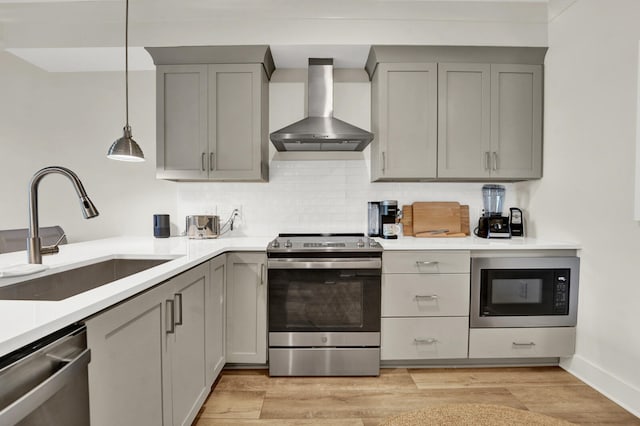 kitchen with stainless steel appliances, sink, wall chimney range hood, pendant lighting, and gray cabinets