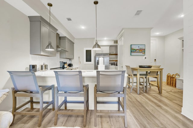 kitchen with kitchen peninsula, wall chimney exhaust hood, pendant lighting, light hardwood / wood-style flooring, and gray cabinets