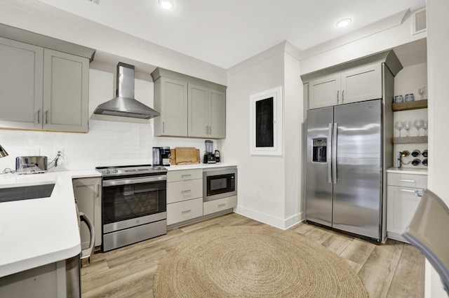 kitchen with gray cabinetry, wall chimney exhaust hood, stainless steel appliances, and light hardwood / wood-style floors