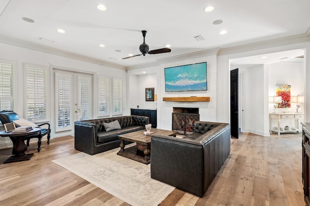 living room featuring a large fireplace, light hardwood / wood-style floors, ceiling fan, and ornamental molding