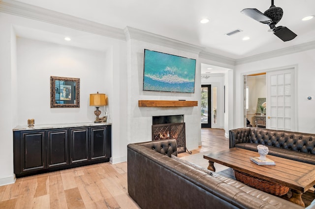 living room featuring light wood-type flooring, a large fireplace, ceiling fan, and crown molding