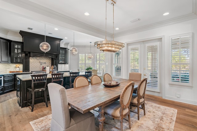 dining room featuring french doors, light wood-type flooring, crown molding, and an inviting chandelier