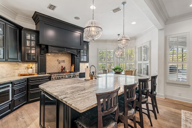 kitchen with an inviting chandelier, a kitchen breakfast bar, hanging light fixtures, light hardwood / wood-style flooring, and an island with sink