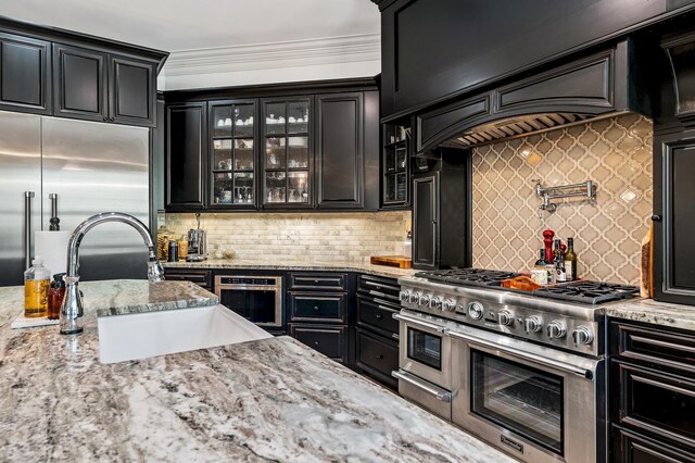 kitchen with sink, crown molding, decorative backsplash, premium appliances, and light stone counters