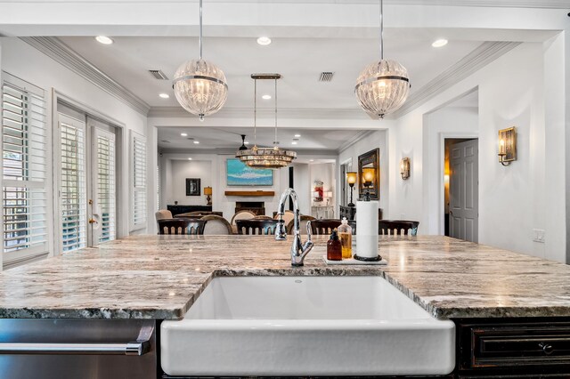 kitchen with decorative light fixtures, light stone countertops, ornamental molding, and sink