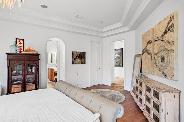 bedroom featuring hardwood / wood-style flooring, a raised ceiling, ornamental molding, and ensuite bathroom