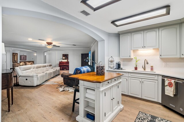 kitchen featuring decorative backsplash, light wood-type flooring, stainless steel dishwasher, ceiling fan, and sink