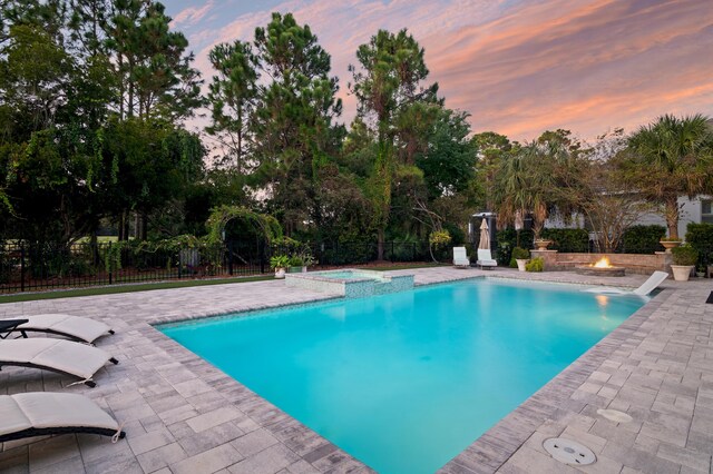 pool at dusk featuring a fire pit, an in ground hot tub, and a patio