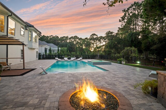 pool at dusk with an in ground hot tub and a patio area