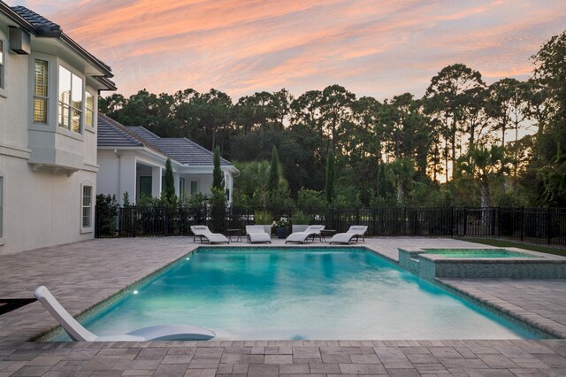 pool at dusk featuring a patio area and an in ground hot tub