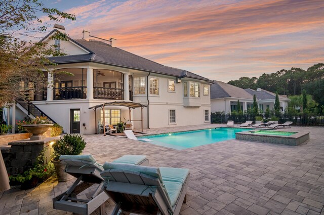 pool at dusk featuring a patio area and an in ground hot tub