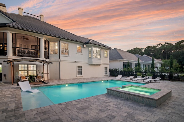 pool at dusk with an in ground hot tub and a patio