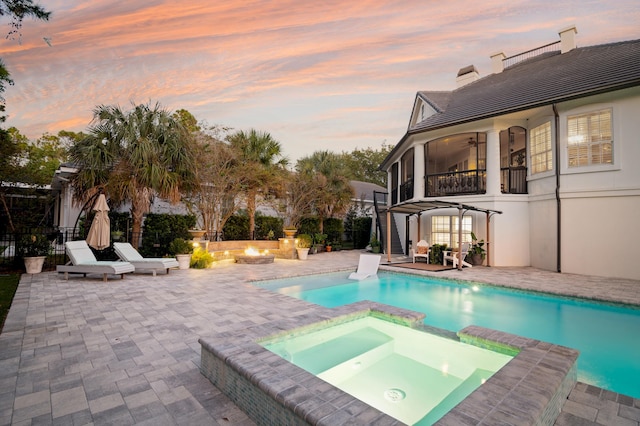 pool at dusk featuring an in ground hot tub, a patio, an outdoor fire pit, and a pergola