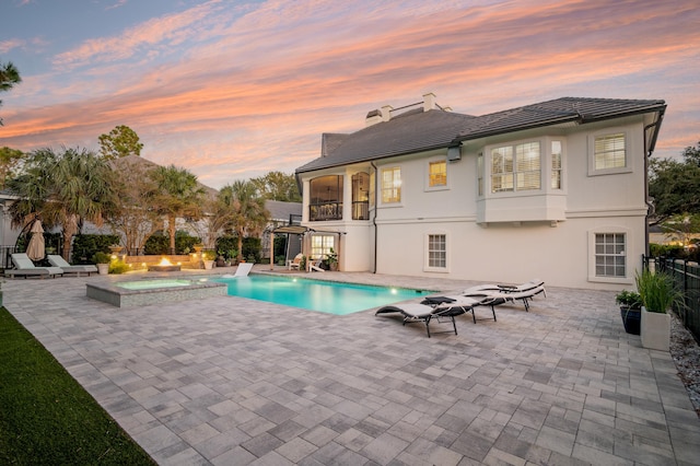 pool at dusk featuring an in ground hot tub and a patio area