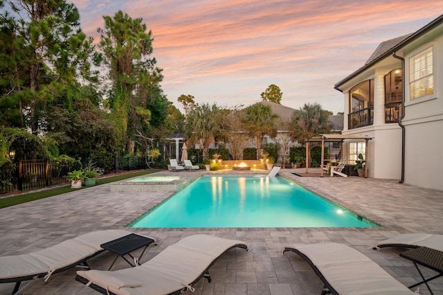 pool at dusk with an in ground hot tub and a patio