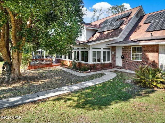 back of house with a wooden deck, a sunroom, a yard, and solar panels