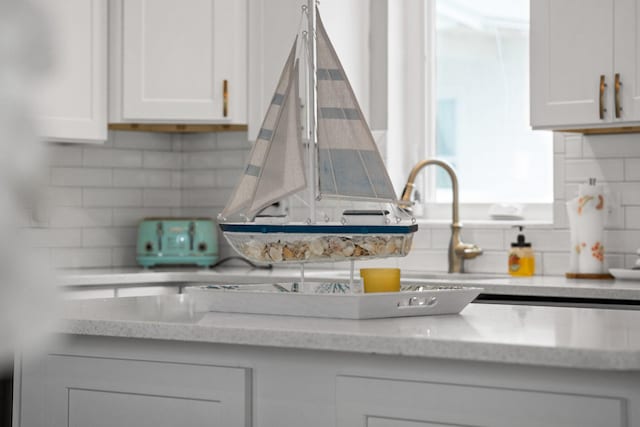 room details featuring tasteful backsplash, white cabinetry, and light stone counters