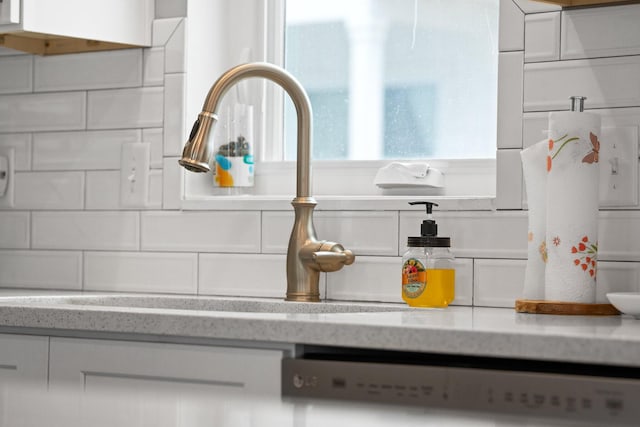 interior details with dishwashing machine, light stone counters, white cabinetry, and backsplash