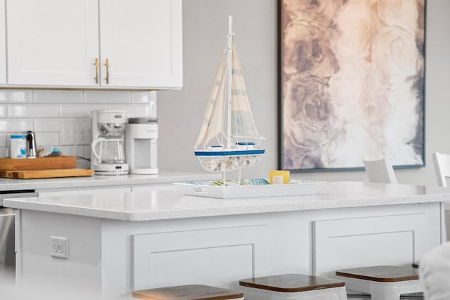 kitchen with decorative backsplash, white cabinetry, stainless steel dishwasher, and light stone counters