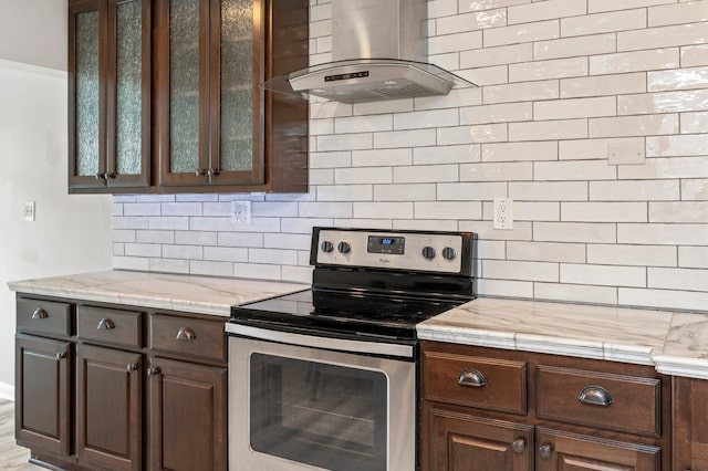 kitchen featuring electric range, decorative backsplash, dark brown cabinetry, and wall chimney range hood