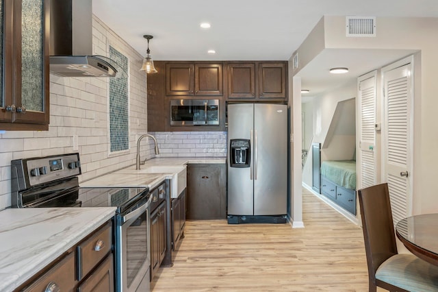 kitchen featuring backsplash, wall chimney exhaust hood, light wood-type flooring, dark brown cabinets, and stainless steel appliances