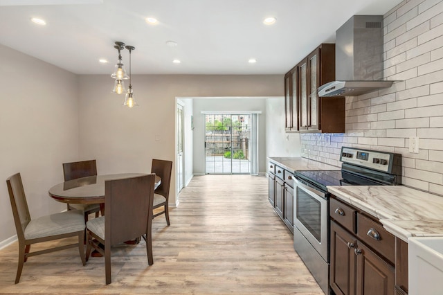 kitchen featuring light stone countertops, wall chimney exhaust hood, decorative light fixtures, light hardwood / wood-style floors, and stainless steel electric range