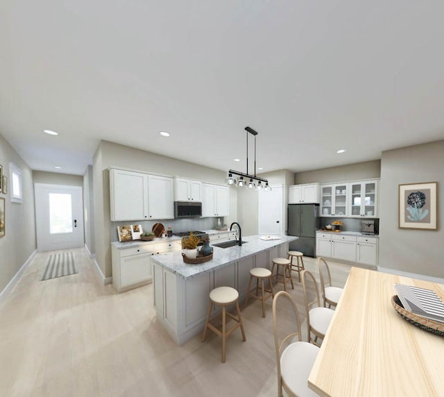 kitchen with white cabinets, stainless steel microwave, freestanding refrigerator, a kitchen bar, and a sink