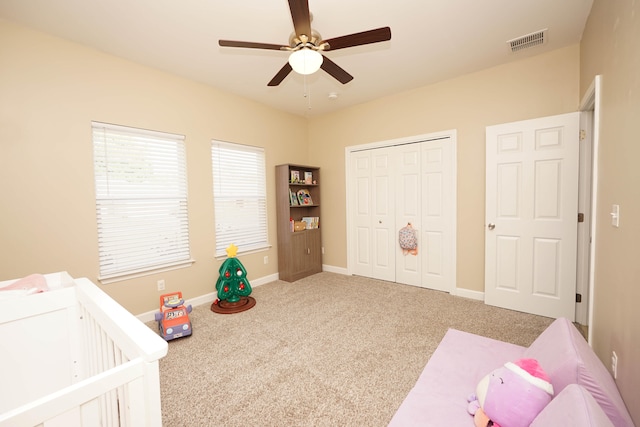 carpeted bedroom featuring ceiling fan, a closet, and a crib