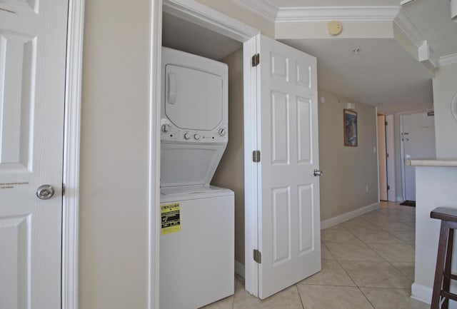 laundry area with light tile patterned floors, ornamental molding, and stacked washer / drying machine