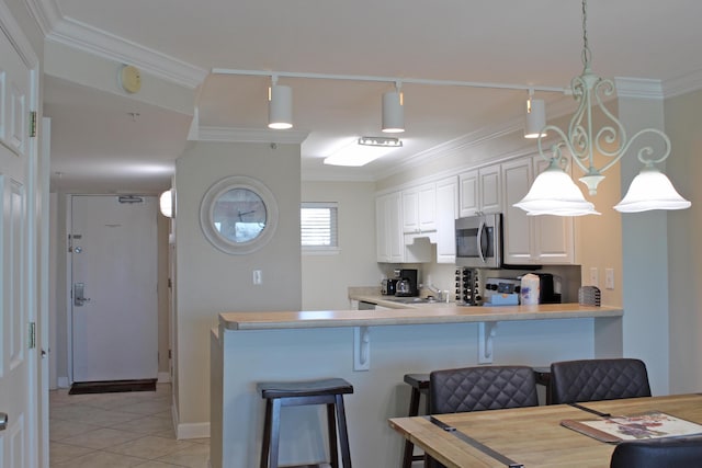 kitchen with decorative light fixtures, white cabinetry, crown molding, and a breakfast bar