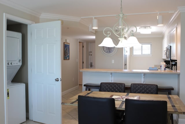 tiled dining space featuring ornamental molding, stacked washer and dryer, and a chandelier