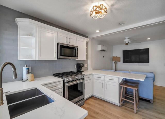 kitchen with white cabinets, an AC wall unit, sink, light hardwood / wood-style flooring, and stainless steel appliances