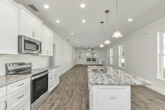 kitchen featuring a center island with sink, sink, ceiling fan, appliances with stainless steel finishes, and white cabinetry