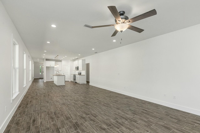 unfurnished living room with ceiling fan, sink, and dark wood-type flooring