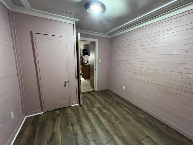 unfurnished bedroom with wooden walls, dark hardwood / wood-style floors, and ornamental molding