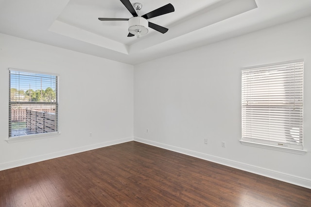 empty room featuring a tray ceiling, ceiling fan, and dark wood-type flooring