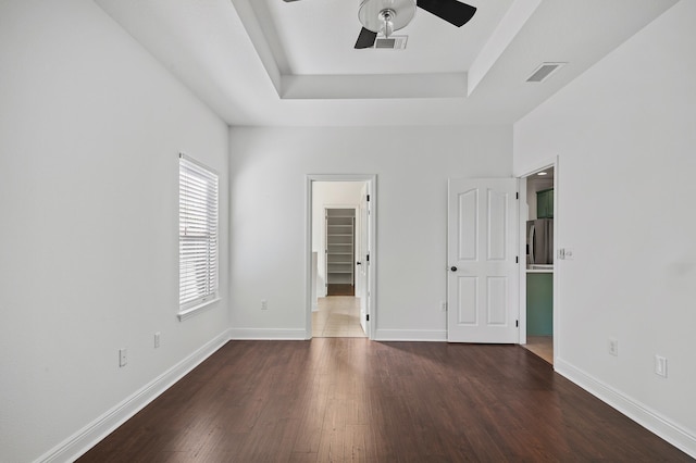 unfurnished bedroom with a walk in closet, dark hardwood / wood-style floors, ceiling fan, a tray ceiling, and a closet